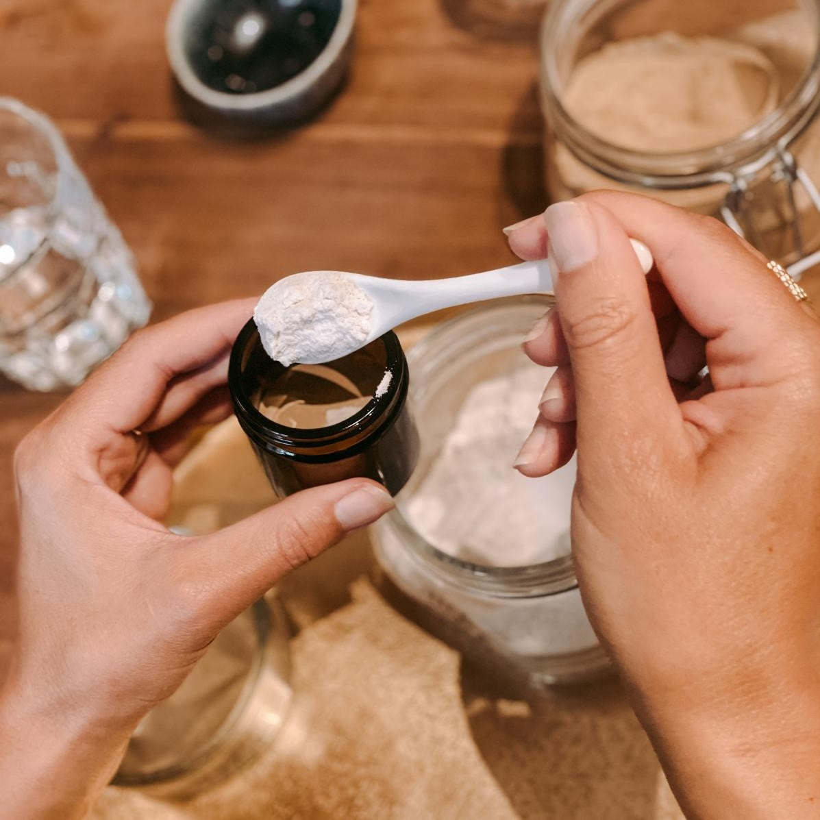 Zwei Hände entnehmen weißes Pulver aus Glas – vegane Masken selbst herstellen.