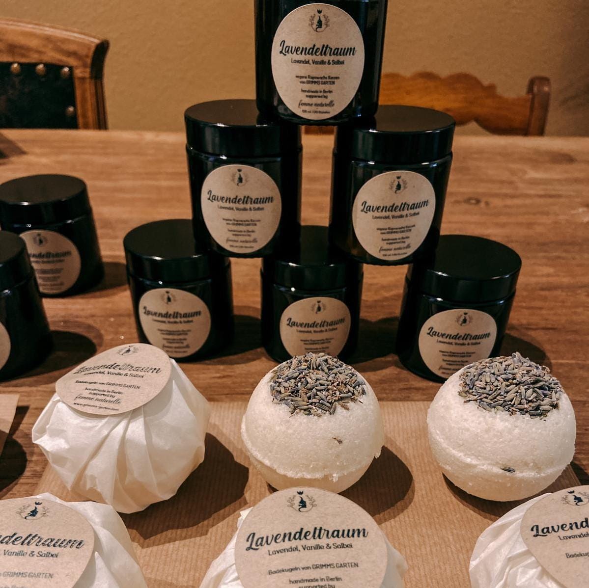 Mehrere verpackte Lavendeltraum Badekugeln mit Duftkerzen im Hintergrund – veganes Pflege-Set.