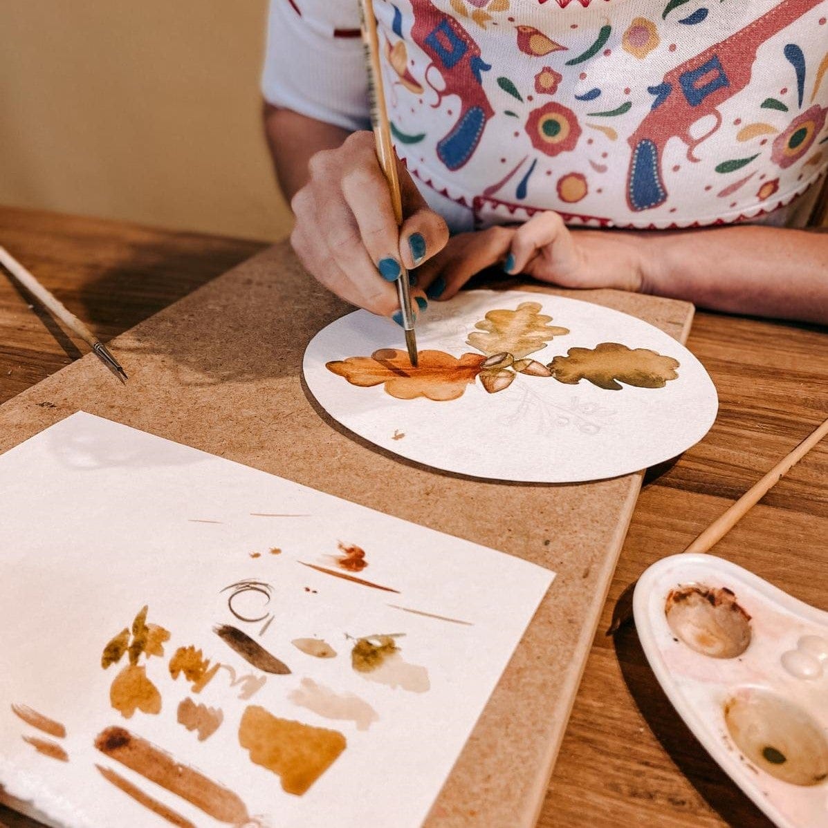 Hände malen mit Pinsel auf Blatt in Orange- und Brauntönen – Herbst Aquarell Workshop.