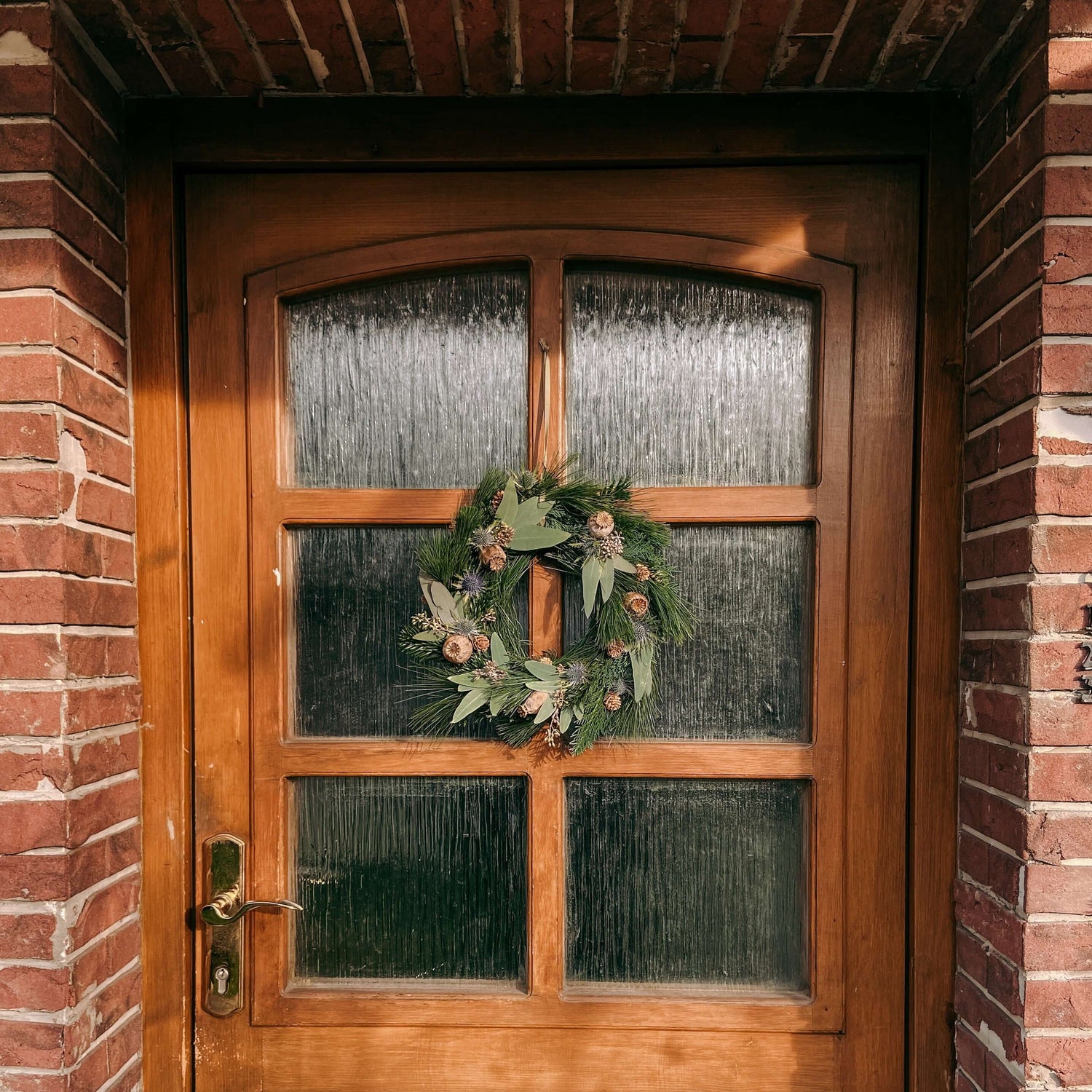 Tür mit hängendem Kranz, Backsteinwand im Hintergrund – weihnachtsdeko, türkranz weihnachten, auch für Firmenevents.