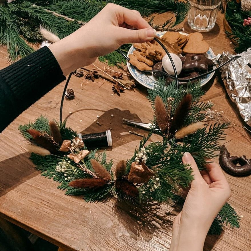 Hand hält fast fertigen Ring, Materialien und Lebkuchen auf Tisch – deko ring weihnachten, diy weihnachtsdeko.