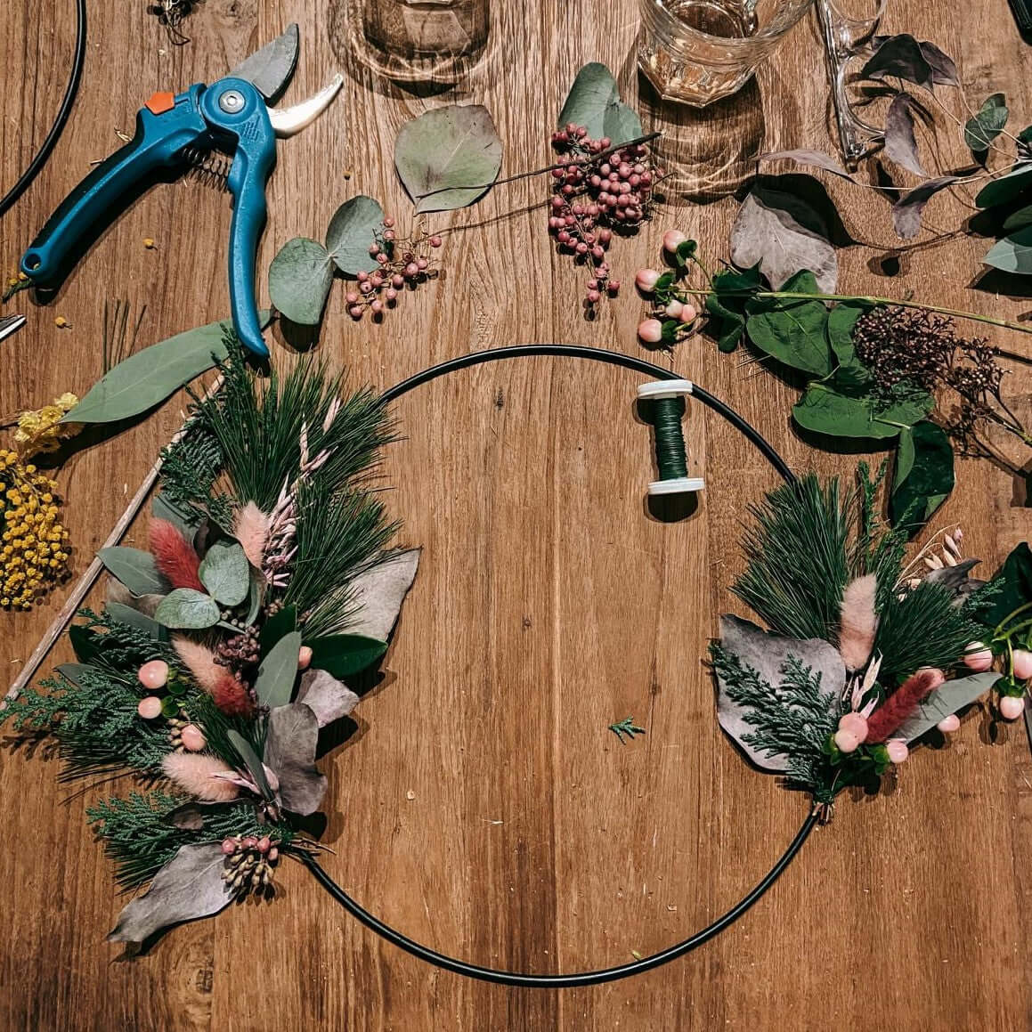 Tisch mit Materialien wie Tannenzweigen, Draht und Trockenblumen – diy weihnachtsdeko, eukalyptus ring.