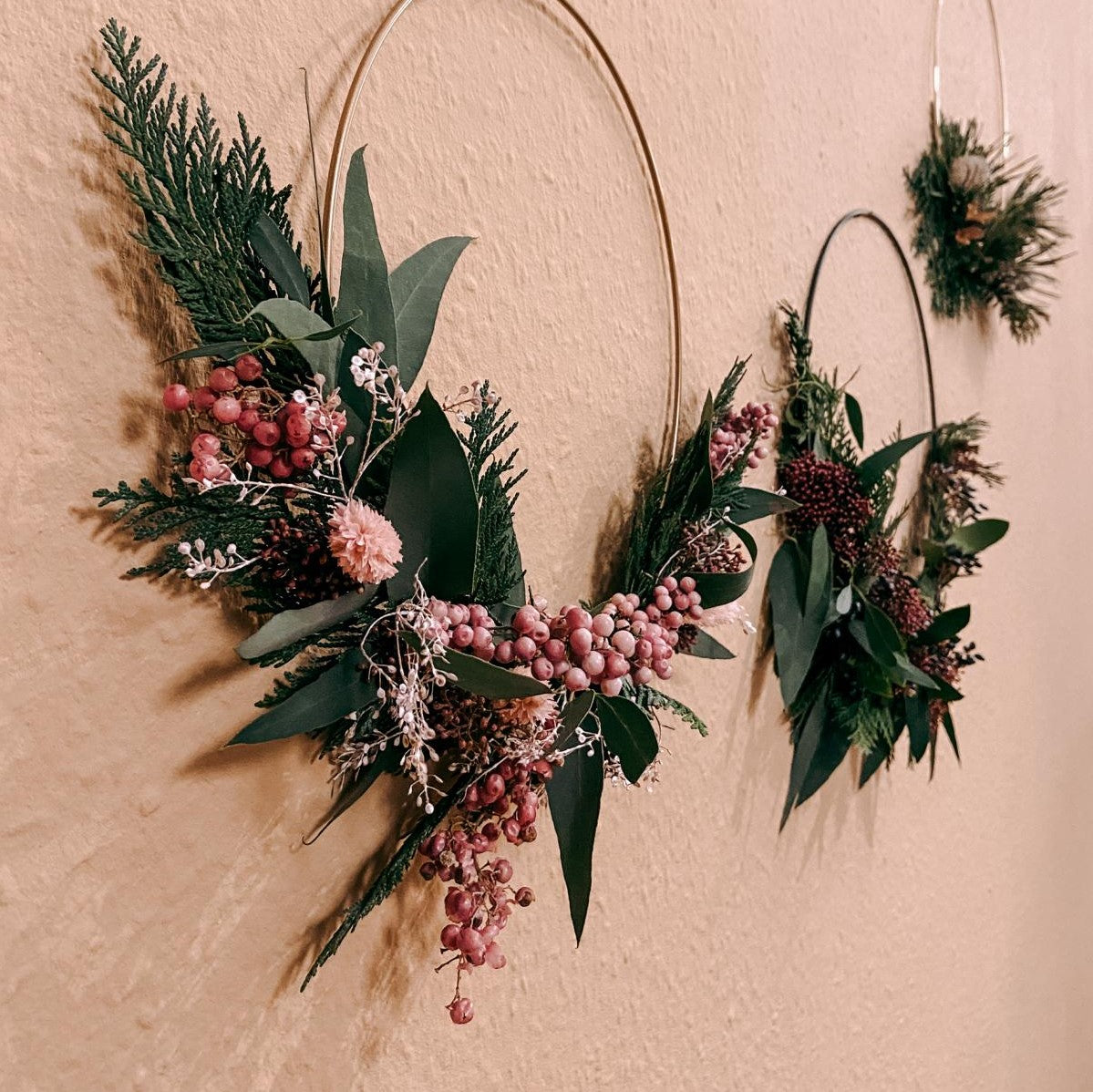 Zwei fertige Deko-Ringe mit rosa Akzenten hängen an Wand – weihnachtsdeko ring, trockenblumen ring.