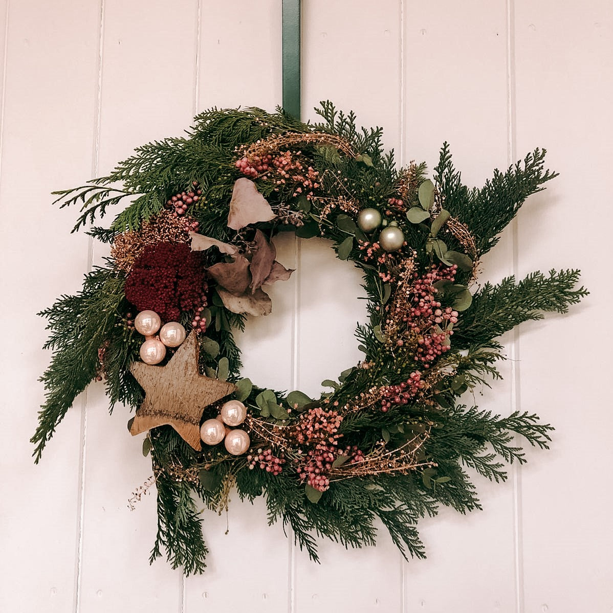 Fertiger Weihnachtskranz hängt an Tür, Nahaufnahme – türkranz weihnachten, weihnachtsdeko, auch für Firmenevents.