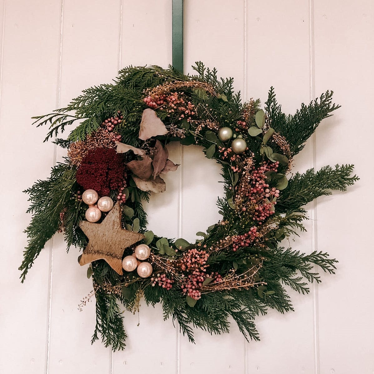 Fertiger Weihnachtskranz hängt an Tür, Nahaufnahme – türkranz weihnachten, weihnachtsdeko, auch für Firmenevents.