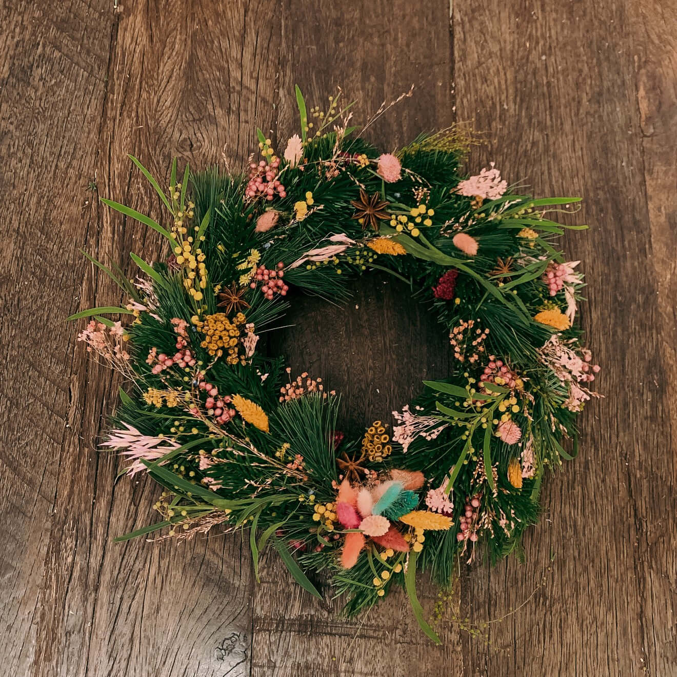 Fertiger Weihnachtskranz auf Holztisch mit Tannenzweigen und bunten Blumen – türkranz weihnachten, auch für Firmenevents.