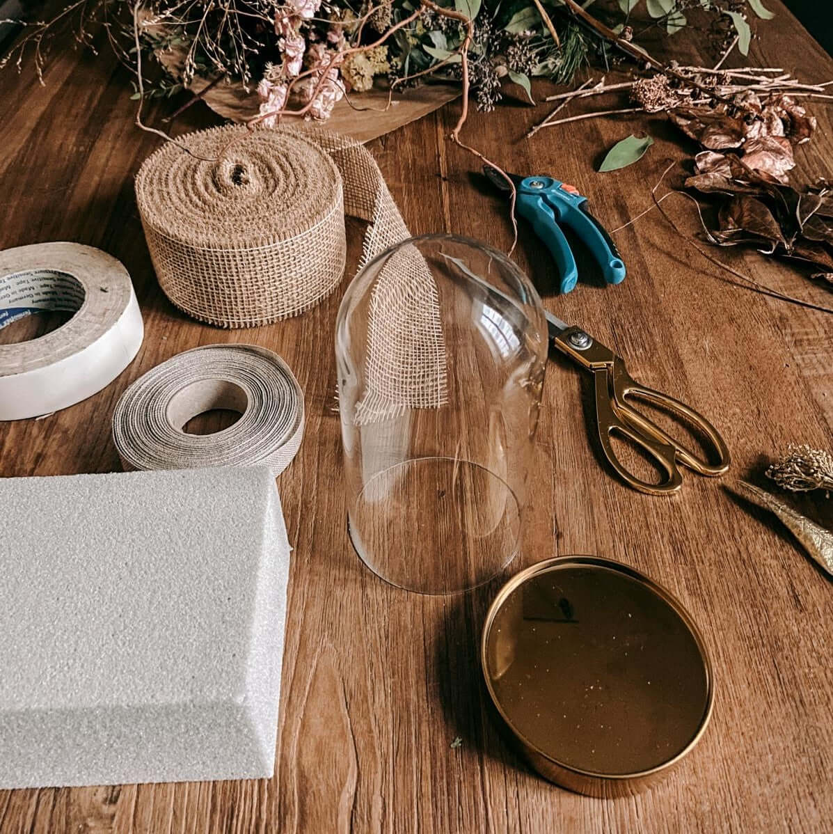 Leere Glasglocke mit Trockenblumen, Garn und Schere auf Holztisch – DIY Boho Deko, Trockenblumen Workshop.