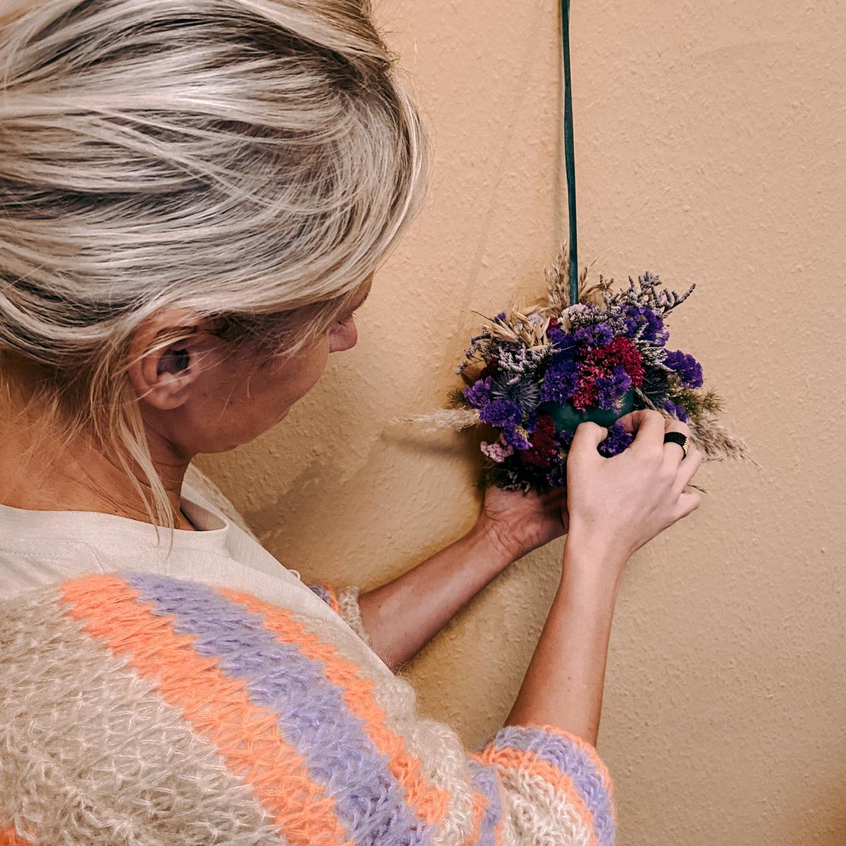 Frau hält FlowerBall in Lila an Wand – kreativer Workshop für frische Blumen.
