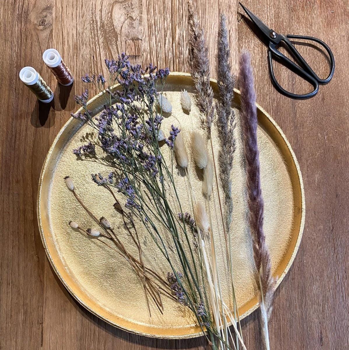 Goldenes Tablett mit Trockenblumen, Schere und Draht im Hintergrund – DIY Trockenblumenring Workshop.
