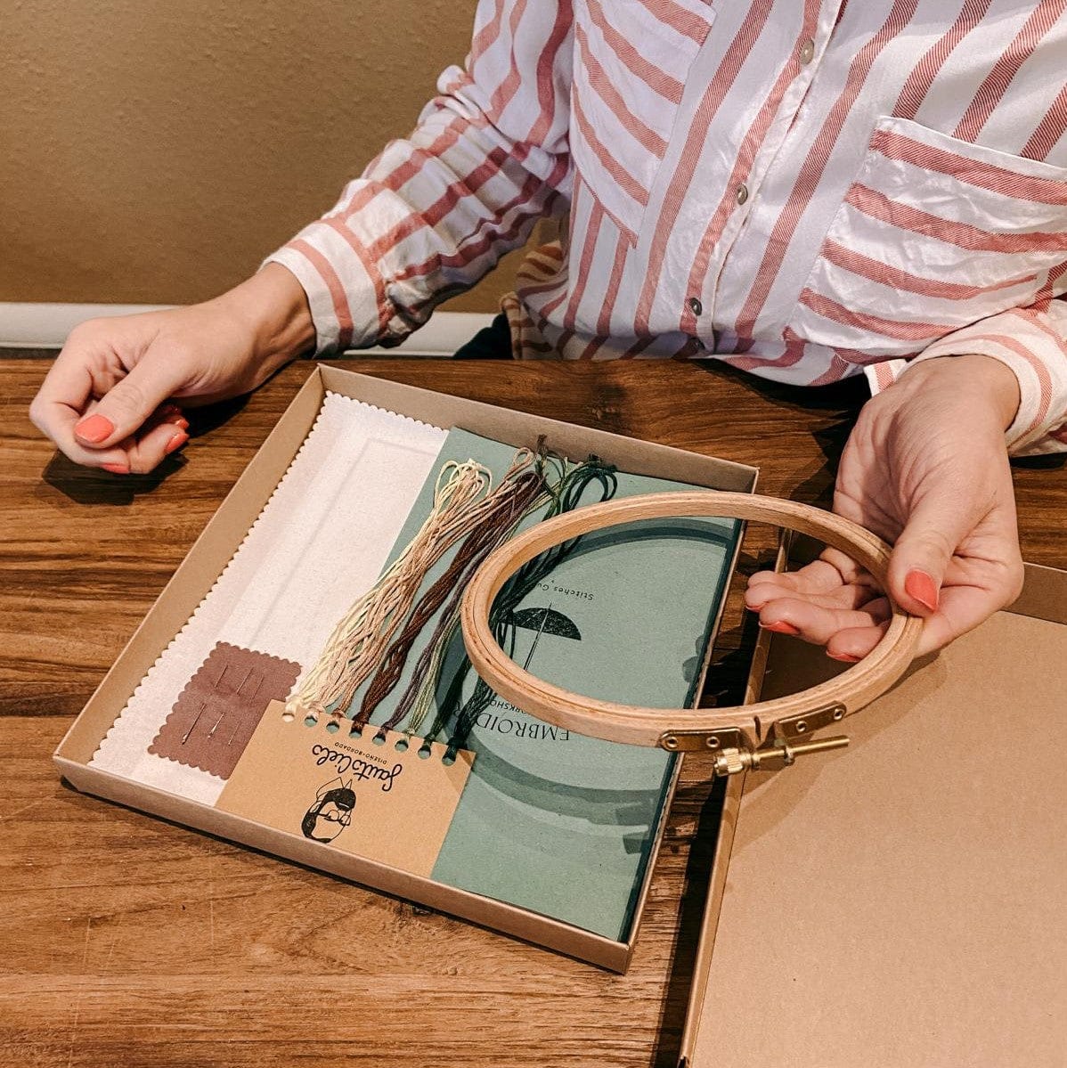 Person hält Workshop-Materialien für Pilz-Stickerei auf Holztisch bereit.