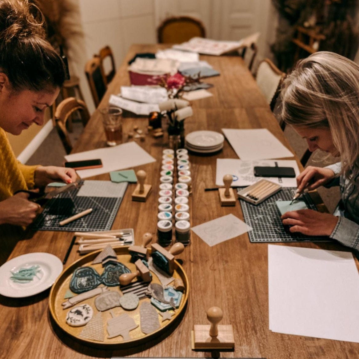 Tisch mit Materialien und zwei Personen beim Stempelschnitzen – diy druck workshop, textildruck, stempel ideen, auch für Firmenevents.