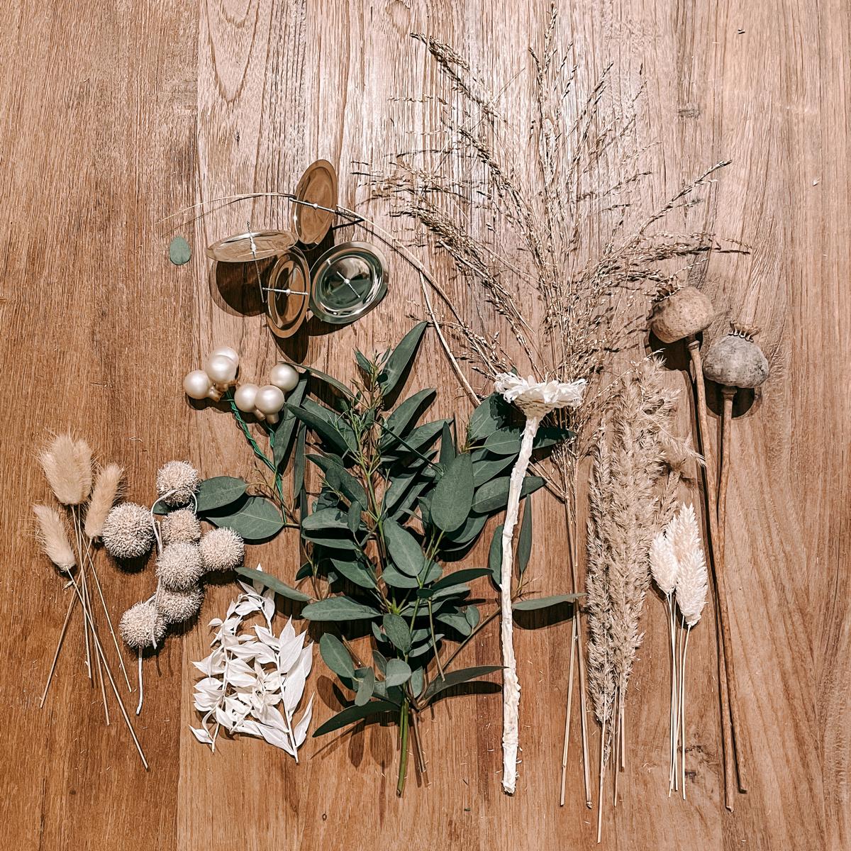 Weiße, beige und grüne Trockenblumen liegen bereit – DIY Box Hänsel Materialien für Adventskranz.