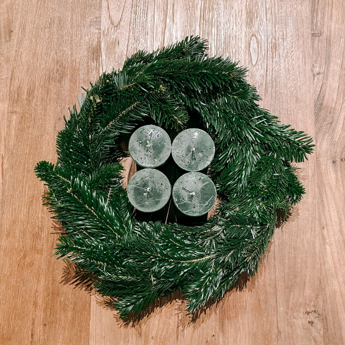 Grüner Adventskranz mit vier Kerzen auf Holztisch – stilvolle Weihnachtsdeko zum Selbermachen.