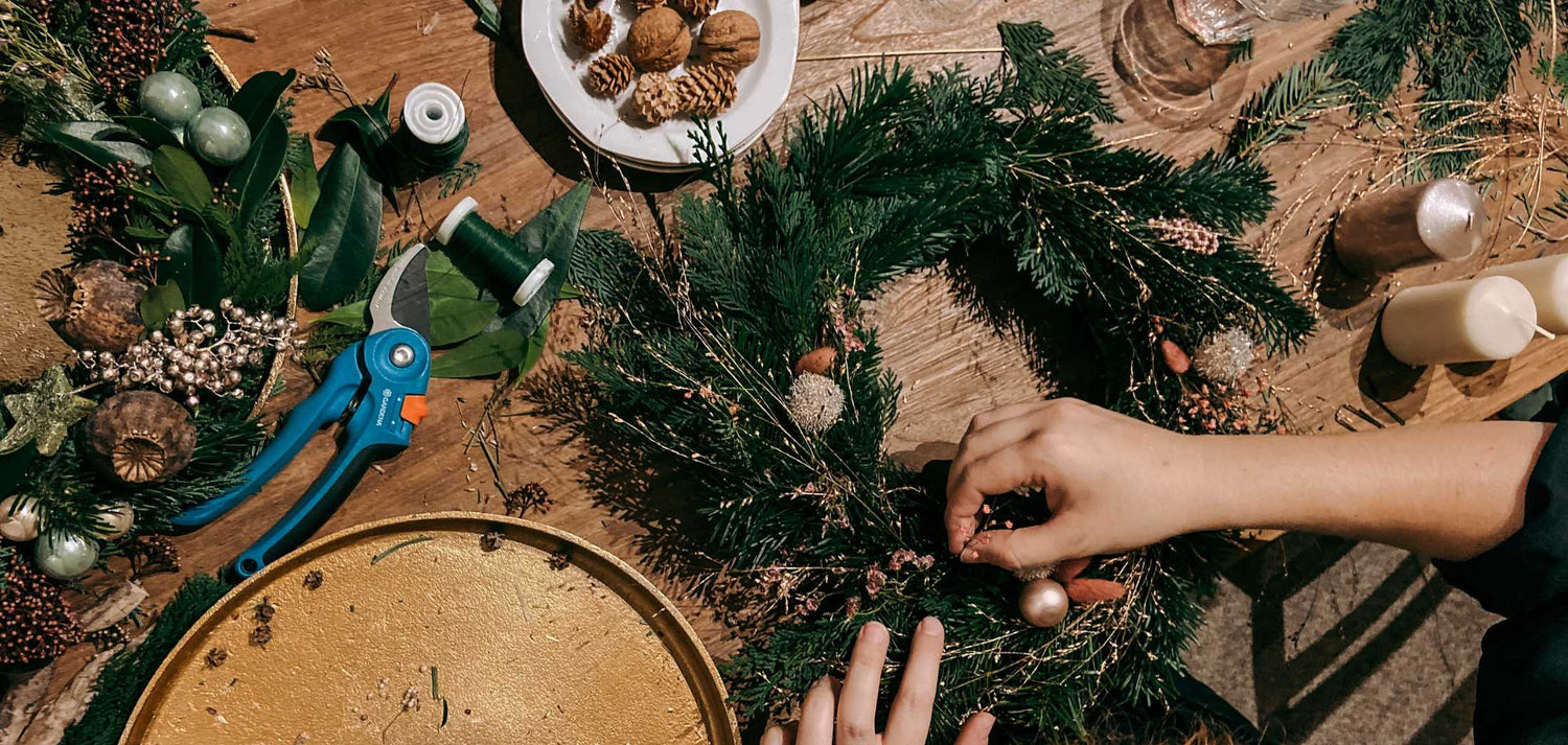 Hand fertigt Adventskranz DIY im GRIMMS GARTEN Workshop – verschiedene Materialien auf Tisch für kreatives Weihnachtsgesteck.