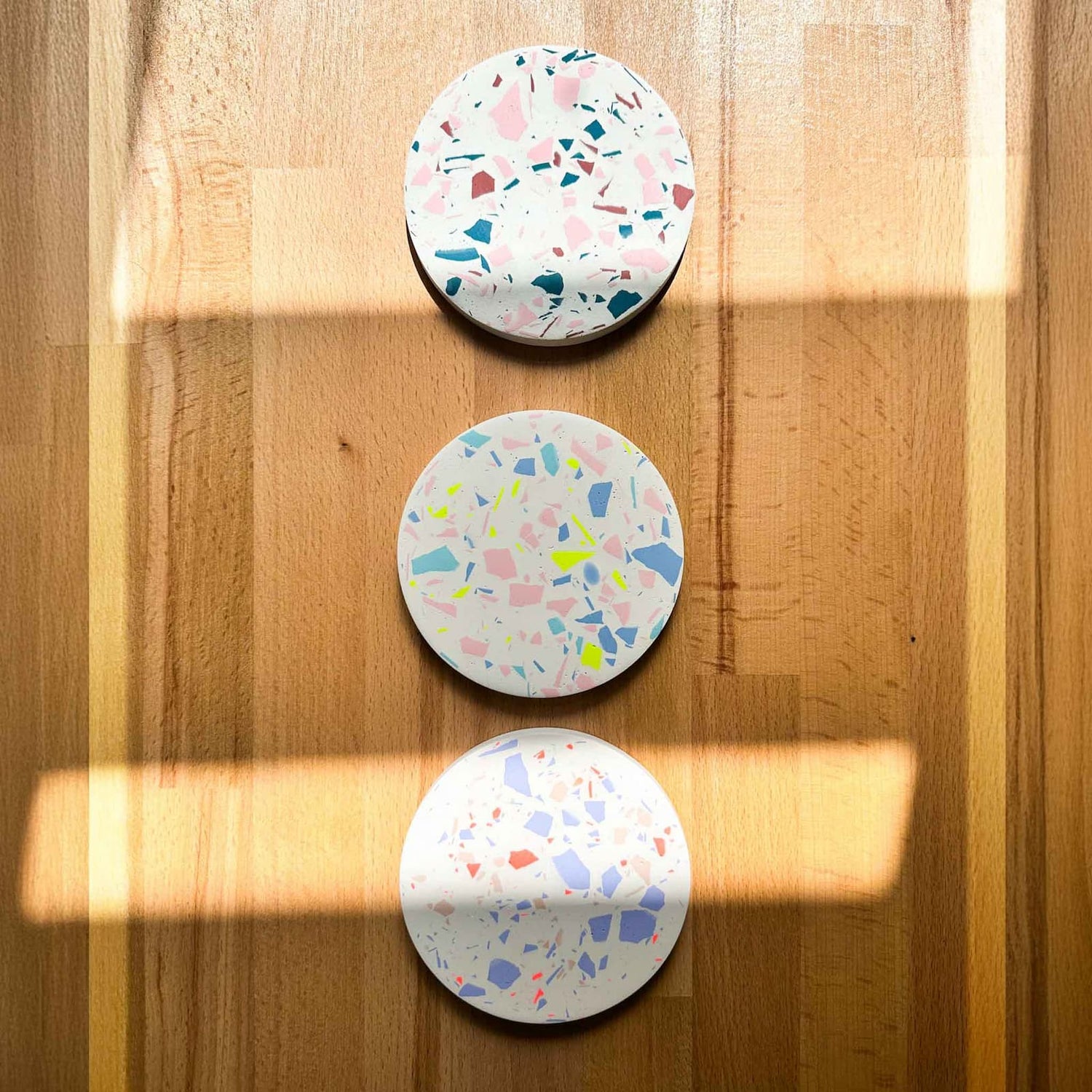 Drei fertige Terrazzo-Untersetzer in verschiedenen Farben dekorativ auf dem Tisch präsentiert