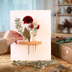 Hand steckt Blumen in Rahmen, rote Blumen schon drinnen – trockenblumen kunstwerk workshop.