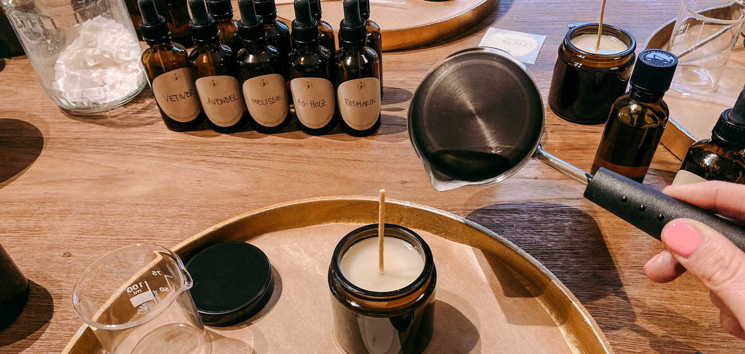 Materialien für Duftkerzen-Workshop auf Tisch, Hand gießt Wachs in Kerze beim GRIMMS GARTEN Workshop.