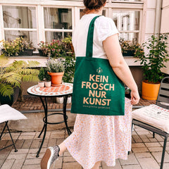 Person trägt nachhaltigen Jutebeutel „KEIN FROSCH NUR KUNST“ aus Baumwolle von Grimms Garten im Alltag.