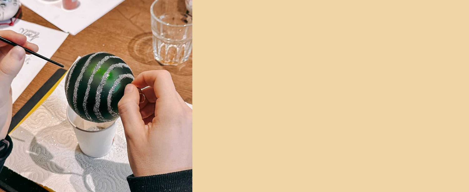 Hand malt silberne Glitzerstreifen auf eine grüne Weihnachtskugel.