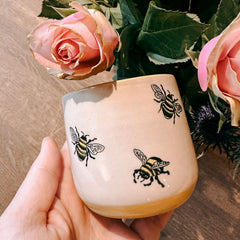 Hand hält bemalte Tasse mit Bienenmotiv beim kreativen Keramik Workshop von GRIMMS GARTEN, DIY Kreativkurs in Berlin