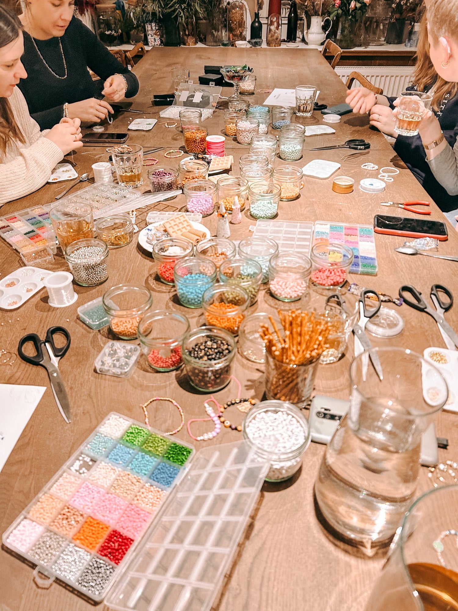 Tisch mit Perlen, Bändern und Materialien während Teilnehmer beim Perlenschmuck Workshop von GRIMMS GARTEN kreative Schmuckstücke basteln, Kreativkurs Berlin