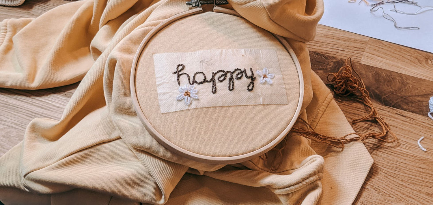 Stickerei „HAPPY“ in Stickrahmen beim Workshop von GRIMMS GARTEN, kreative Handarbeit und DIY-Bastelspaß.