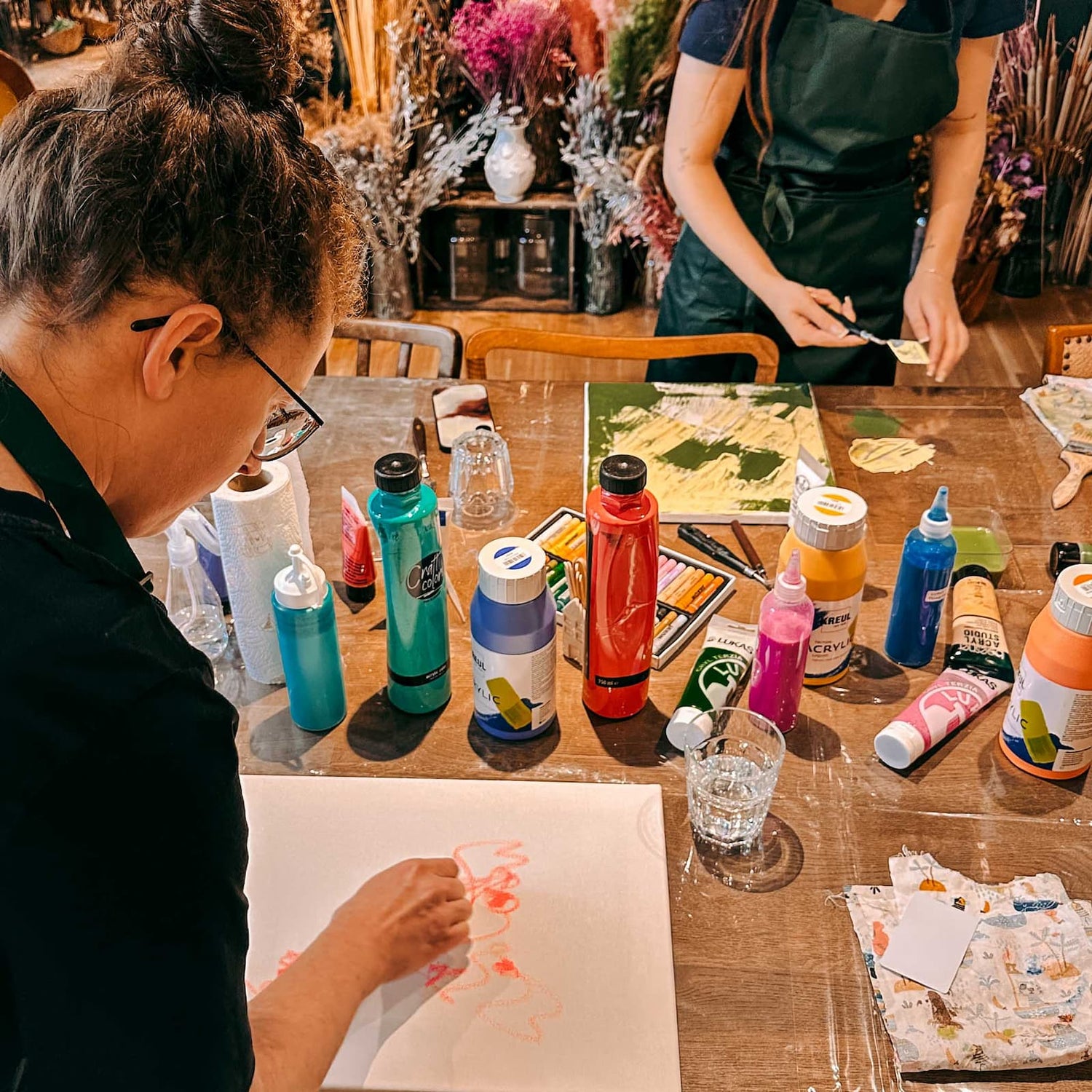 Zwei Personen malen mit Acrylfarben und Wachsmalstiften auf Leinwänden beim Abstract Painting Workshop von GRIMMS GARTEN Berlin