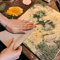Hand presst Wellpappe mit Farbe auf grün gelb bemalte Leinwand beim Abstract Painting Workshop von GRIMMS GARTEN Berlin