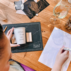 Frau malt Schriftzug mit Porzellanmarker auf einen Becher beim Tassen bemalen Workshop von GRIMMS GARTEN Berlin

