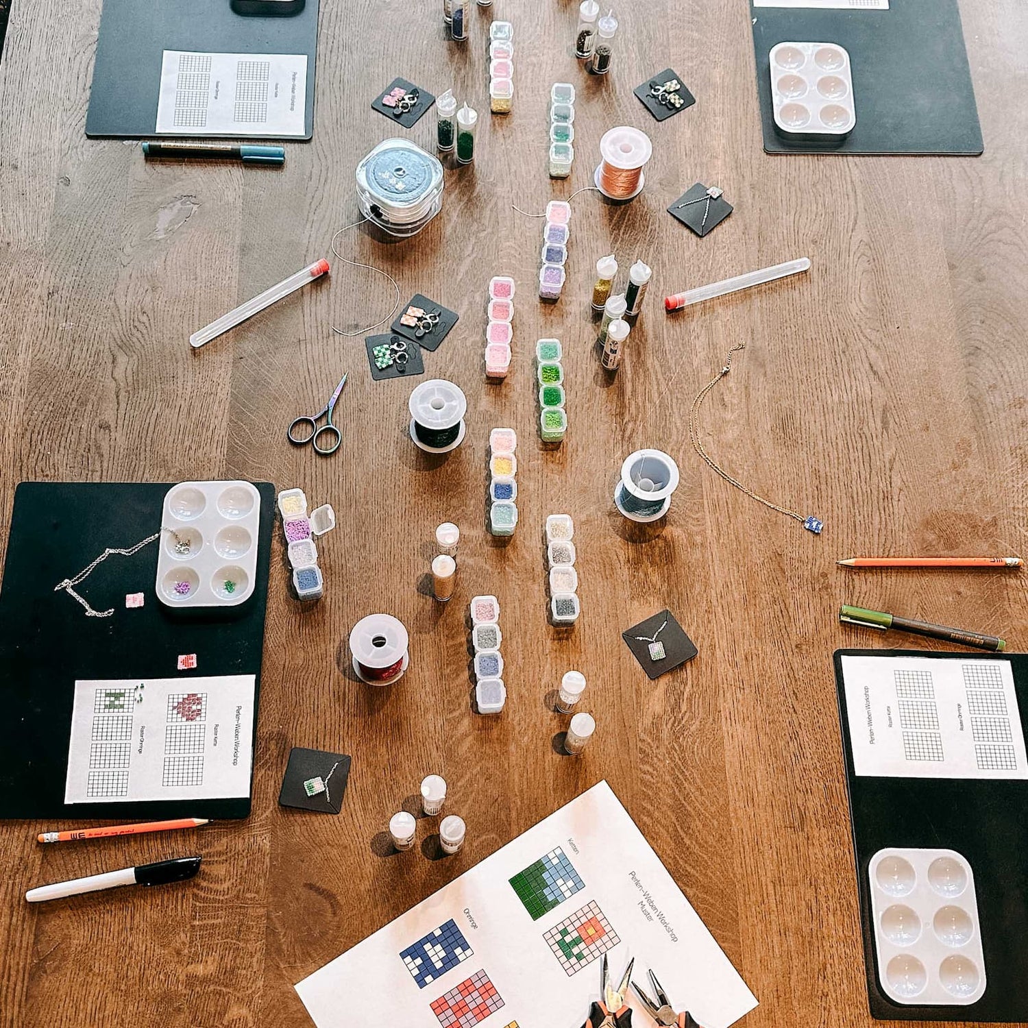 Tisch mit Materialien für Perlenschmuck wie bunte Perlen, Bänder, Schälchen und Vorlagen beim DIY Schmuck Workshop von GRIMMS GARTEN, Kreativkurs in Berlin