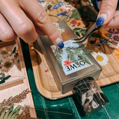 Hände kleben Trockenblume auf Parfum Flakon im kreativen DIY Workshop von GRIMMS GARTEN Berlin
