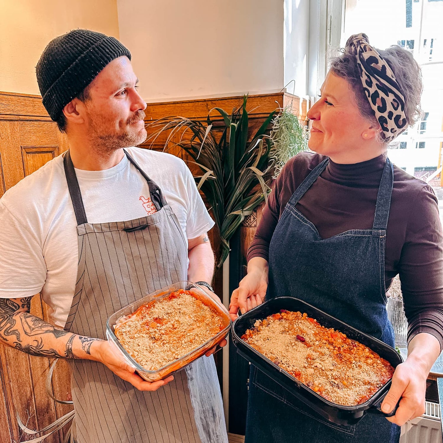 Zwei Personen halten gemeinsam eine fertige Lasagne in den Händen beim Batch Cooking Workshop von GRIMMS GARTEN, Meal Prep Kochkurs in Berlin