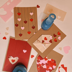 Mit Stanzer gestanzte Herzformen neben fertigen Postkarten in Rosa und Rot beim kreativen Postkarten Workshop von GRIMMS GARTEN, DIY Kurs in Berlin