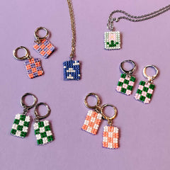 Viele bunte Perlenohrringe mit unterschiedlichen Motiven sowie zwei Halsketten auf lila Hintergrund aus dem DIY Perlenschmuck Workshop von GRIMMS GARTEN, Kreativkurs Berlin