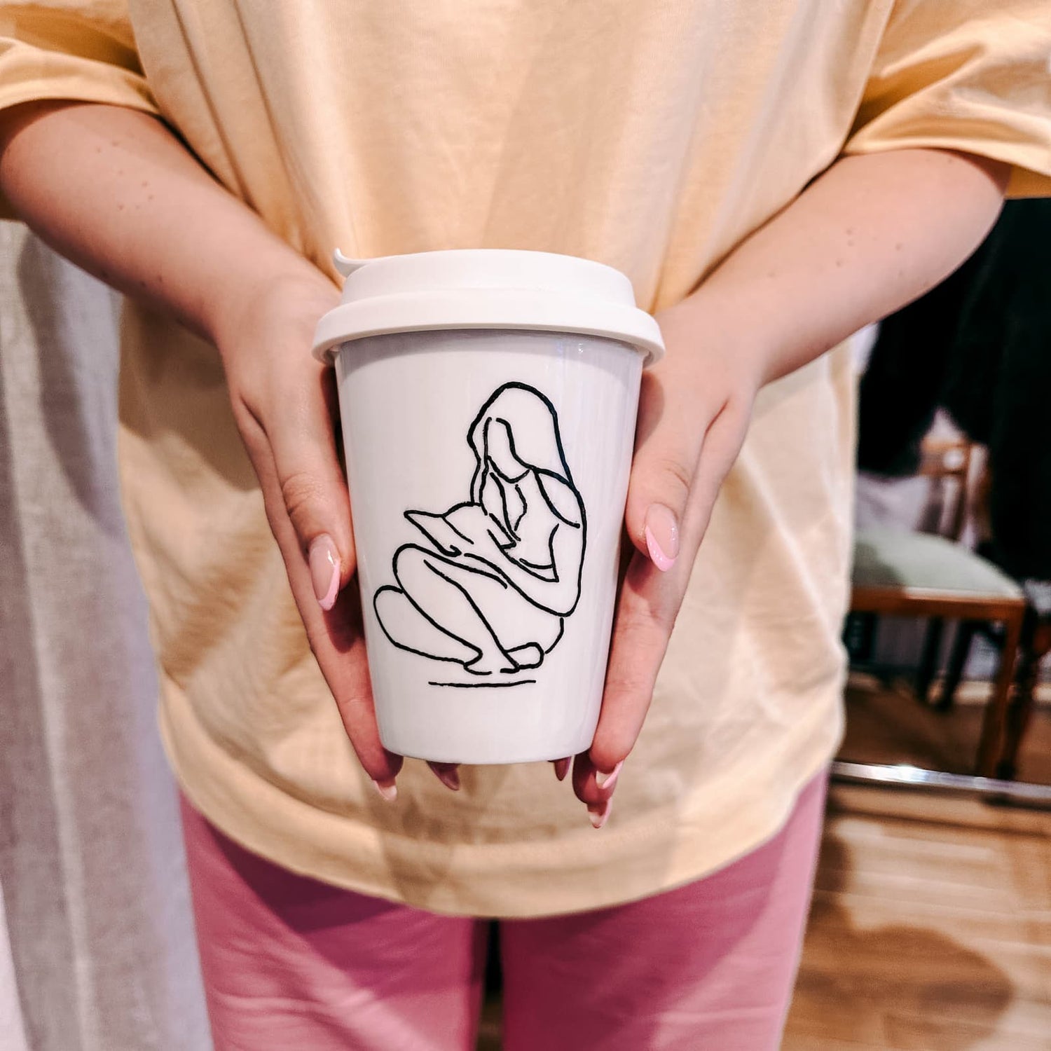 Zwei Hände halten handbemalten Becher mit Frauenmotiv beim Tassen bemalen Workshop von GRIMMS GARTEN Berlin
