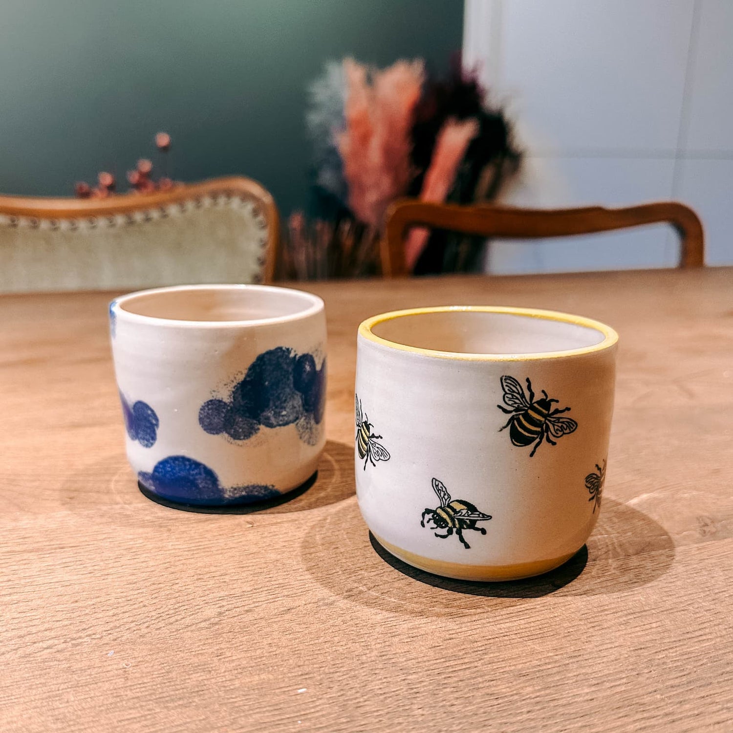 Zwei fertig bemalte Tassen mit Wolken- und Bienen-Motiv, kreative Workshop-Ergebnisse