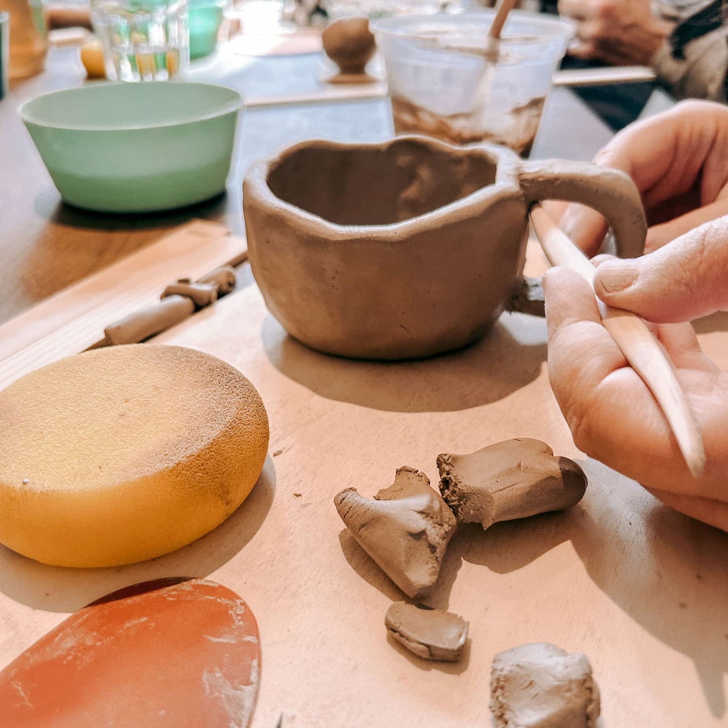 Person formt Henkel an einer Tasse mit Holzstab beim Töpferkurs von GRIMMS GARTEN, kreativer Keramik Workshop und DIY Kurs in Berlin