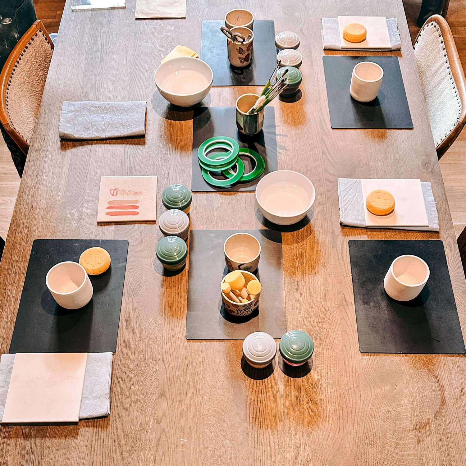 Tisch mit vier fertigen Arbeitsstationen und Materialien zum Keramikbecher bemalen – DIY Keramik Workshop Berlin
