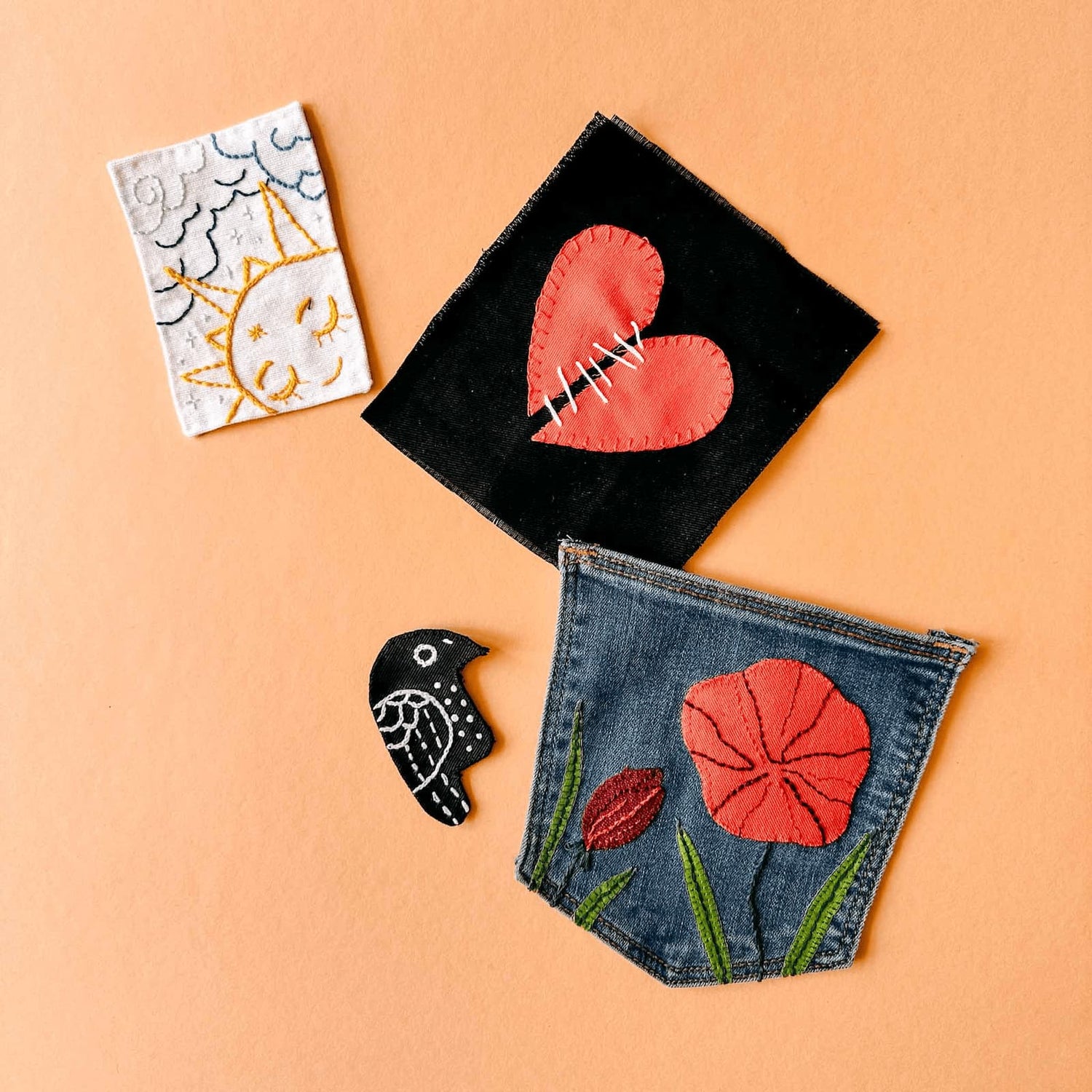Verschiedene gestickte Patches und Vogelvorlage– Herz, Blumenwiese auf blauem Stoff sowie Sonne und Wolken auf weißem Stoff beim Patches nähen Workshop von GRIMMS GARTEN in Berlin