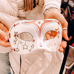 Zwei Hände halten weiße DIY Maske mit roten Sternen beim kreativen Masken Workshop von GRIMMS GARTEN, Teamevent in Berlin