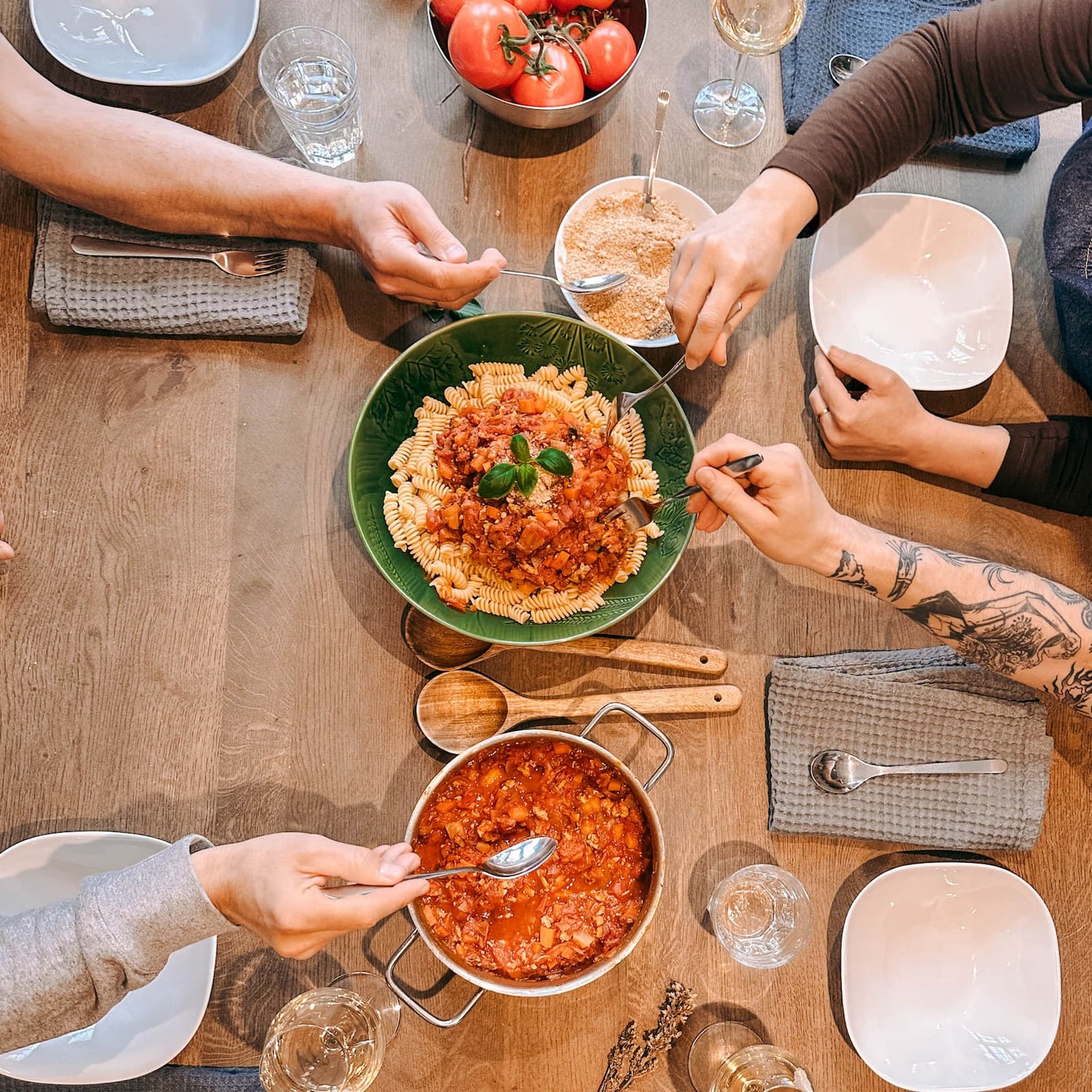 Fertiges Nudelgericht in der Mitte, umgeben von Soße und Händen mit Gabeln beim Batch Cooking Workshop von GRIMMS GARTEN, Meal Prep Kochkurs in Berlin
