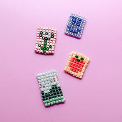 Vier handgemachte Perlenanhänger mit verschiedenen Motiven auf lila Hintergrund aus dem DIY Perlenschmuck Workshop von GRIMMS GARTEN, Kreativkurs in Berlin