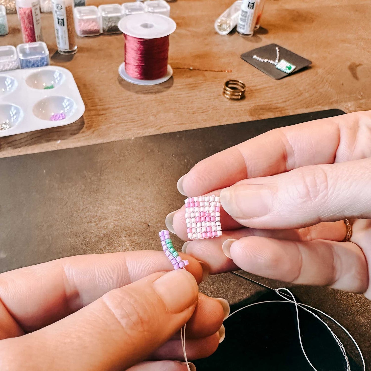 Hand fädelt bunte Perlen auf ein Band, um einen Anhänger zu gestalten, beim DIY Perlenschmuck Workshop von GRIMMS GARTEN, Kreativkurs in Berlin