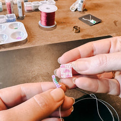 Hand fädelt bunte Perlen auf ein Band, um einen Anhänger zu gestalten, beim DIY Perlenschmuck Workshop von GRIMMS GARTEN, Kreativkurs in Berlin