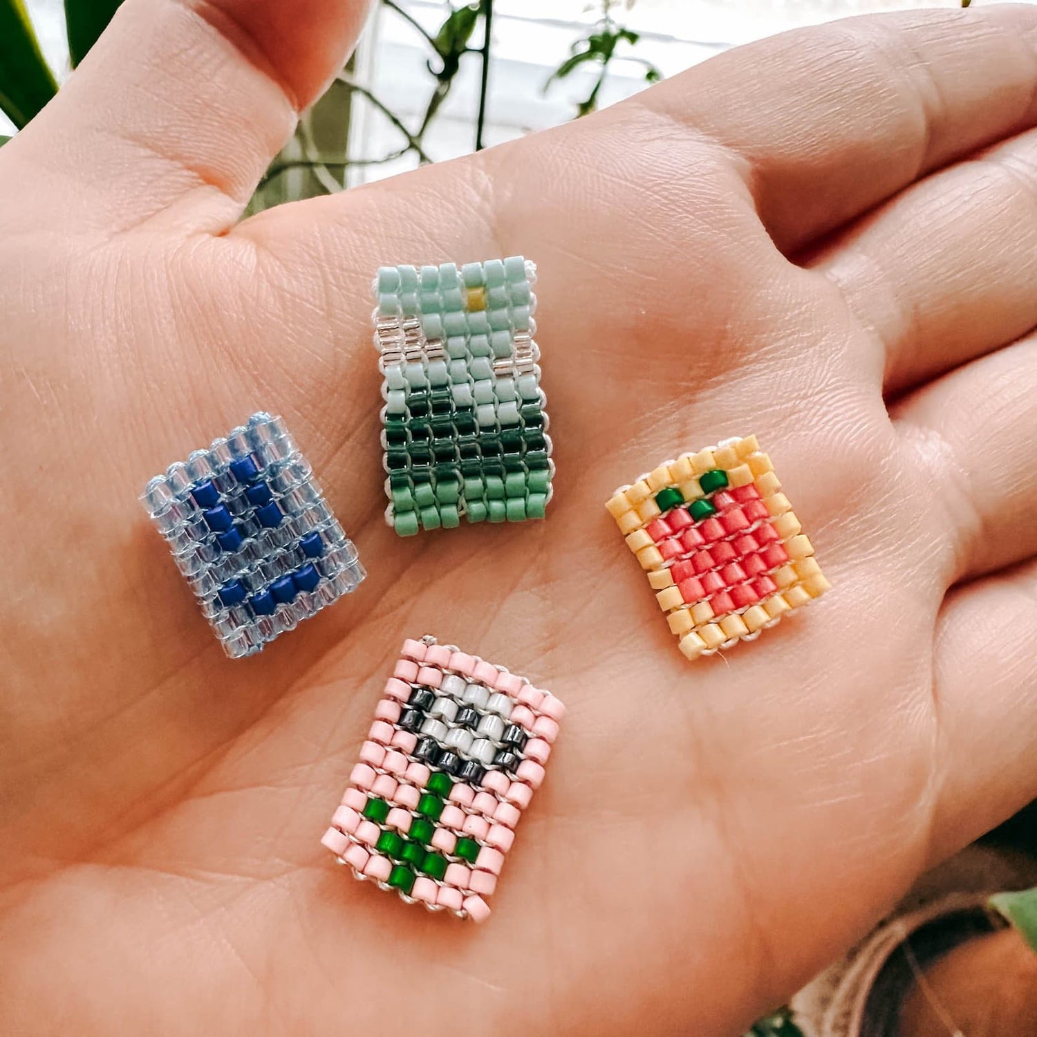 Hand hält vier verschiedene Perlenanhänger mit unterschiedlichen Motiven in Nahaufnahme beim DIY Perlenschmuck Workshop von GRIMMS GARTEN in Berlin