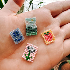 Hand hält vier verschiedene Perlenanhänger mit unterschiedlichen Motiven in Nahaufnahme beim DIY Perlenschmuck Workshop von GRIMMS GARTEN in Berlin