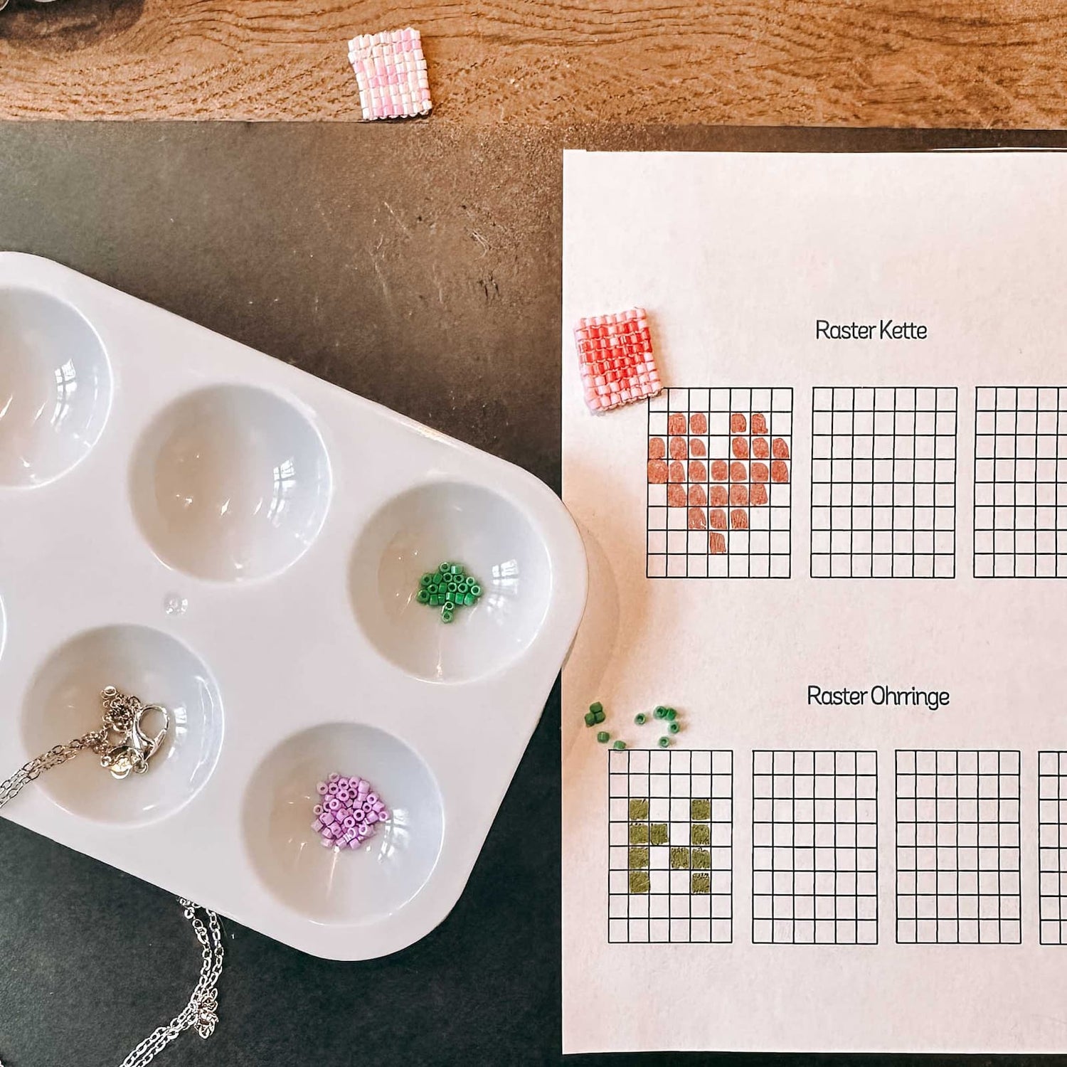 Grüne und lila Schmuckperlen in einer Schale neben Papier-Vorlagen mit Buchstabe N und Herz beim DIY Perlenschmuck Workshop von GRIMMS GARTEN in Berlin