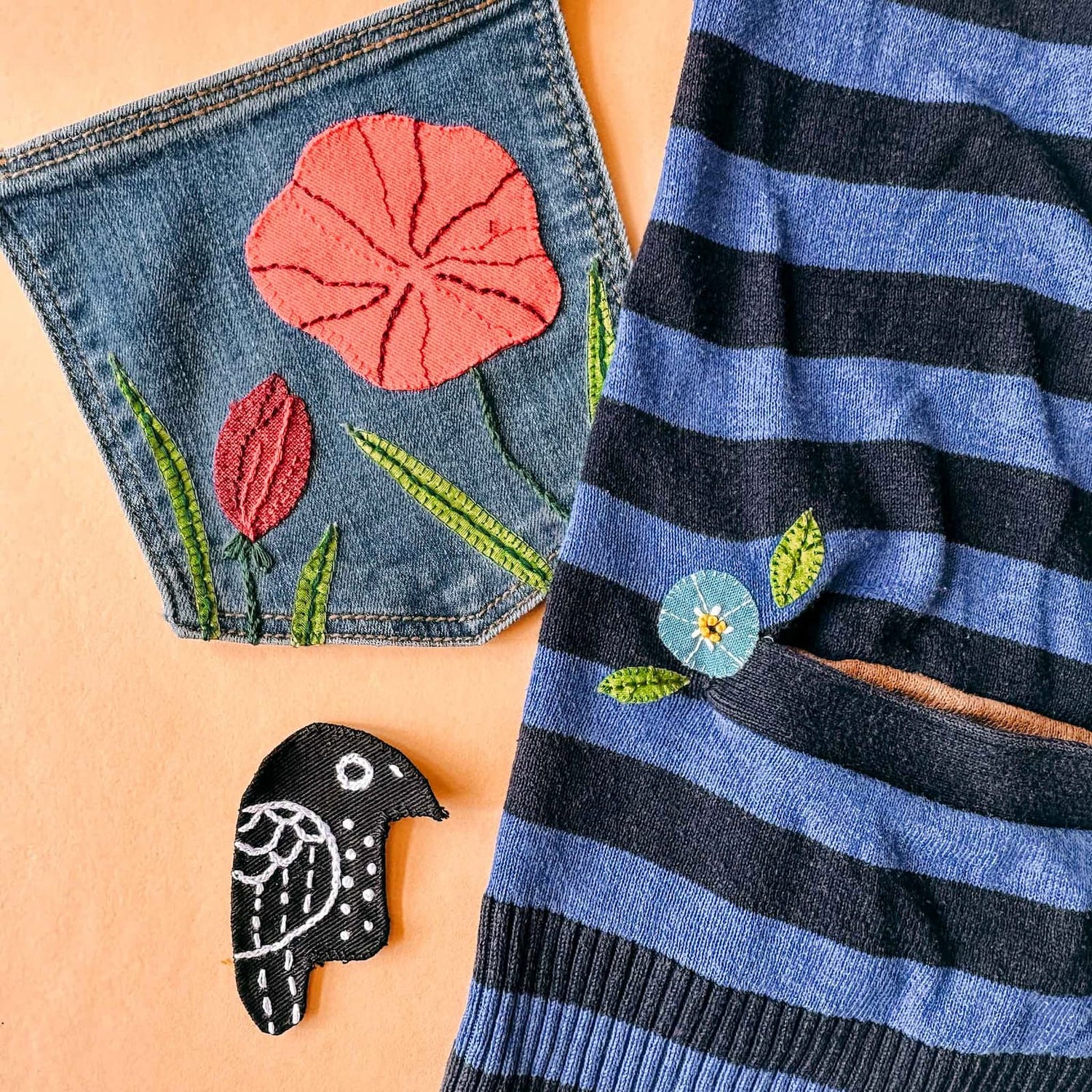 Vorlage mit Vogelmotiv neben Jeansstoff mit gestickter Blumenwiese und Blume auf gestreiftem Shirt beim Patches nähen Workshop von GRIMMS GARTEN in Berlin