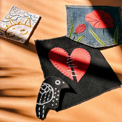Verschiedene gestickte Patches – Herz, Blumenwiese auf blauem Stoff sowie Sonne und Wolken auf weißem Stoff beim Patches nähen Workshop von GRIMMS GARTEN in Berlin