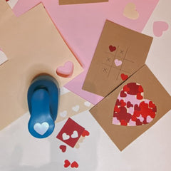 Herzstanzer neben Papier mit ausgestanzten Formen und zwei braunen Postkarten mit roten und rosa Herzmotiven beim kreativen Postkarten Workshop von GRIMMS GARTEN in Berlin